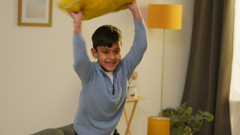 Disruptive-Young-Boy-Behaving-Badly-At-Home-Jumping-On-Sofa-And-Throwing-Cushions-Around-Lounge-2